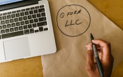 Close-up of hand writing 'Form LLC' on craft paper beside a laptop, indicating business planning.