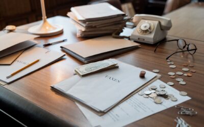 Close-up of an office desk with tax documents, coins, glasses, and an old phone, symbolizing finance and organization.