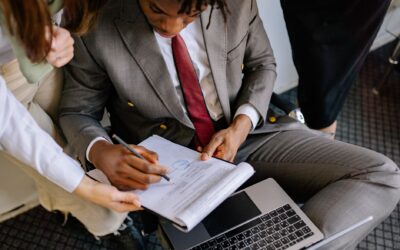 A businessman in a suit signing a contract with colleagues' assistance.